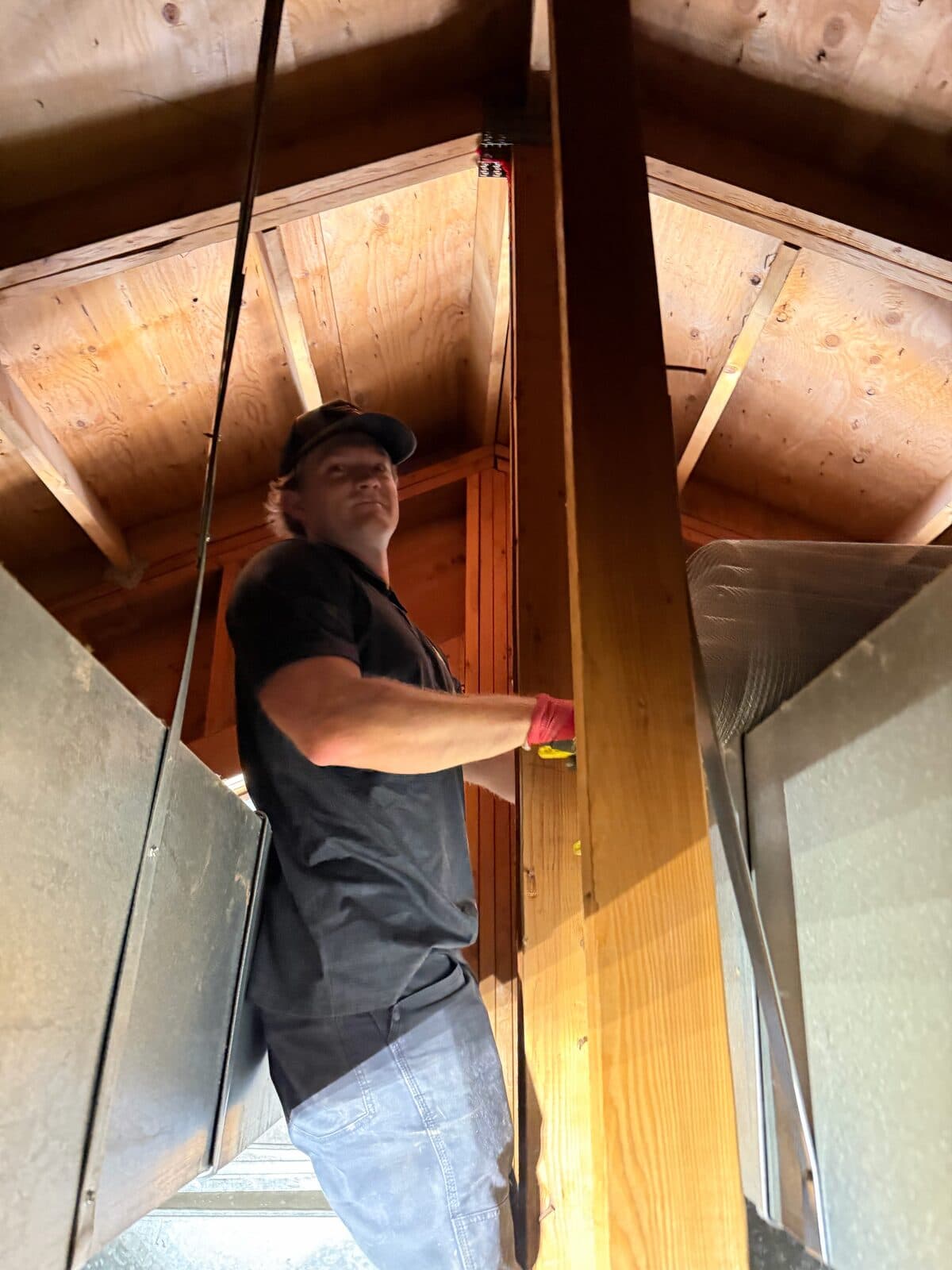 Technician standing in a wood attic beside framing and ductwork, looking up during an inspection