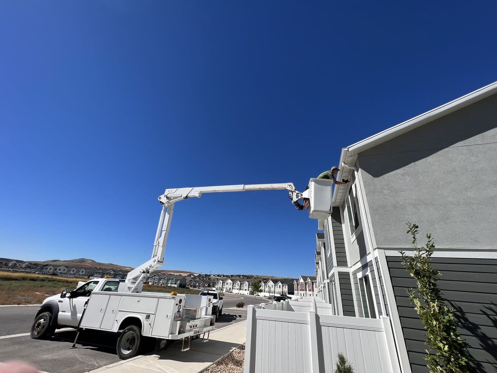 White boom truck with a technician in the bucket working the fascia of gray townhomes under a bright blue sky