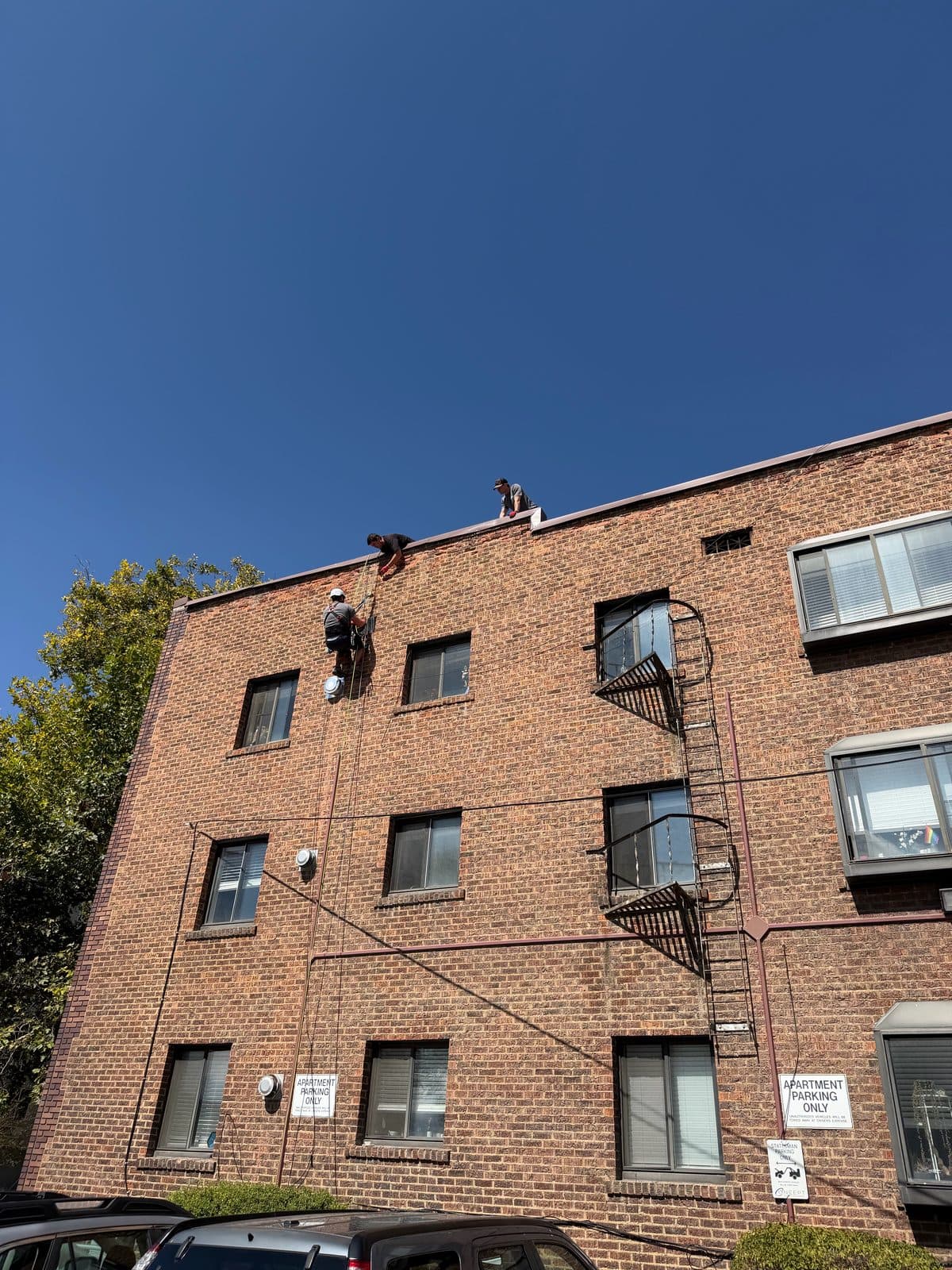 Brick apartment building with technicians on ropes and the roof under a clear blue sky