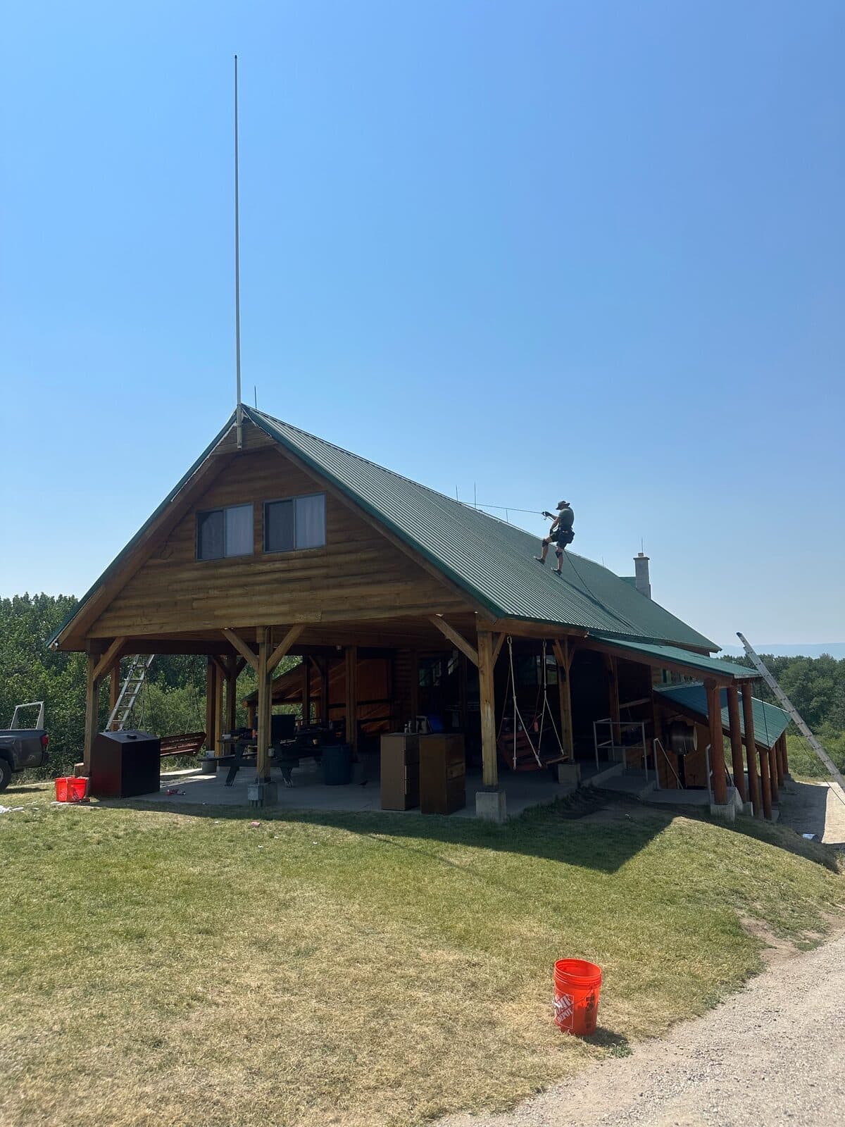 Sunny wood cabin with a green metal roof and a technician working on the roof above an open porch