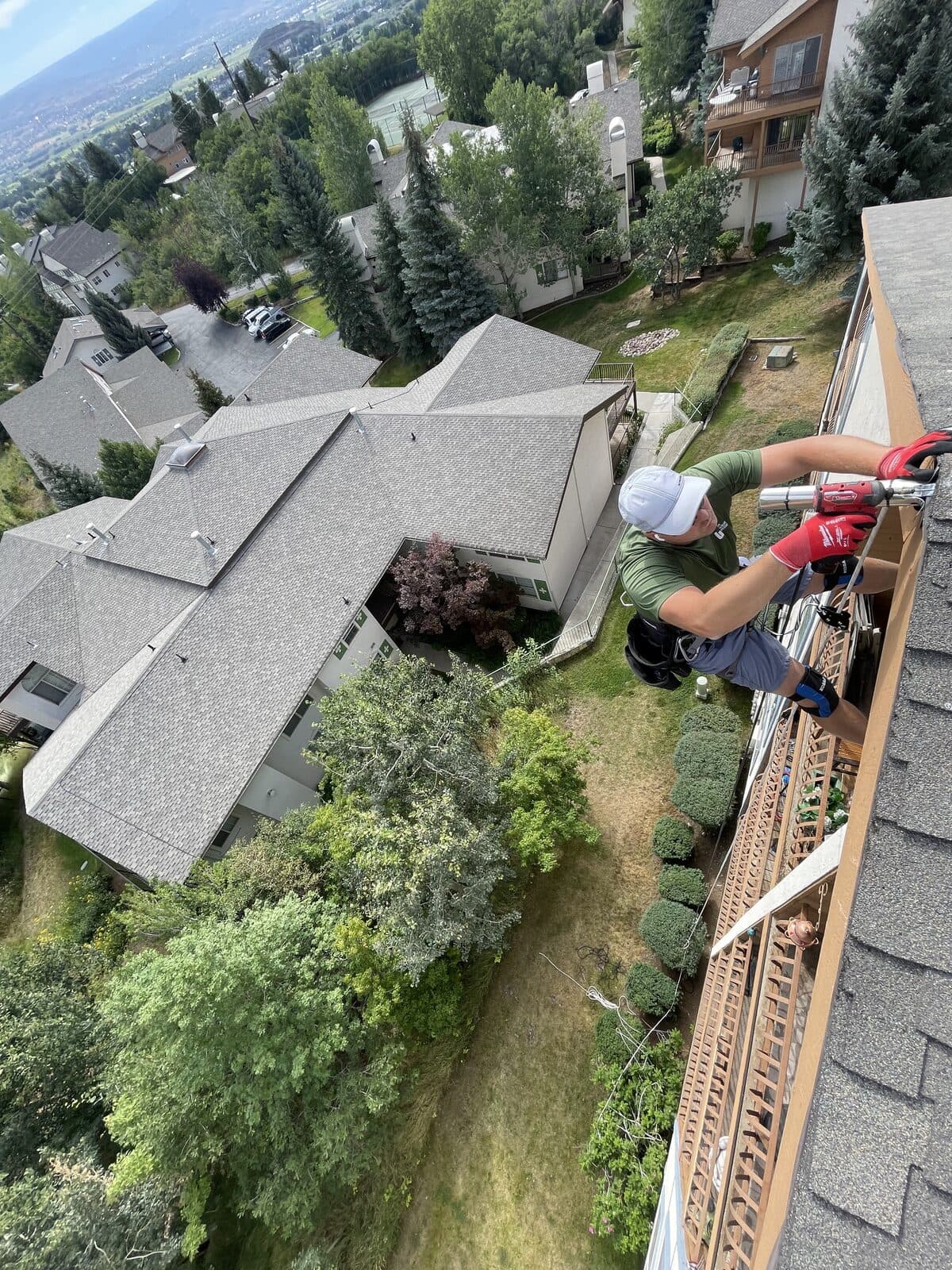 Harness work at a roof edge above balconies overlooking a neighborhood and mountains