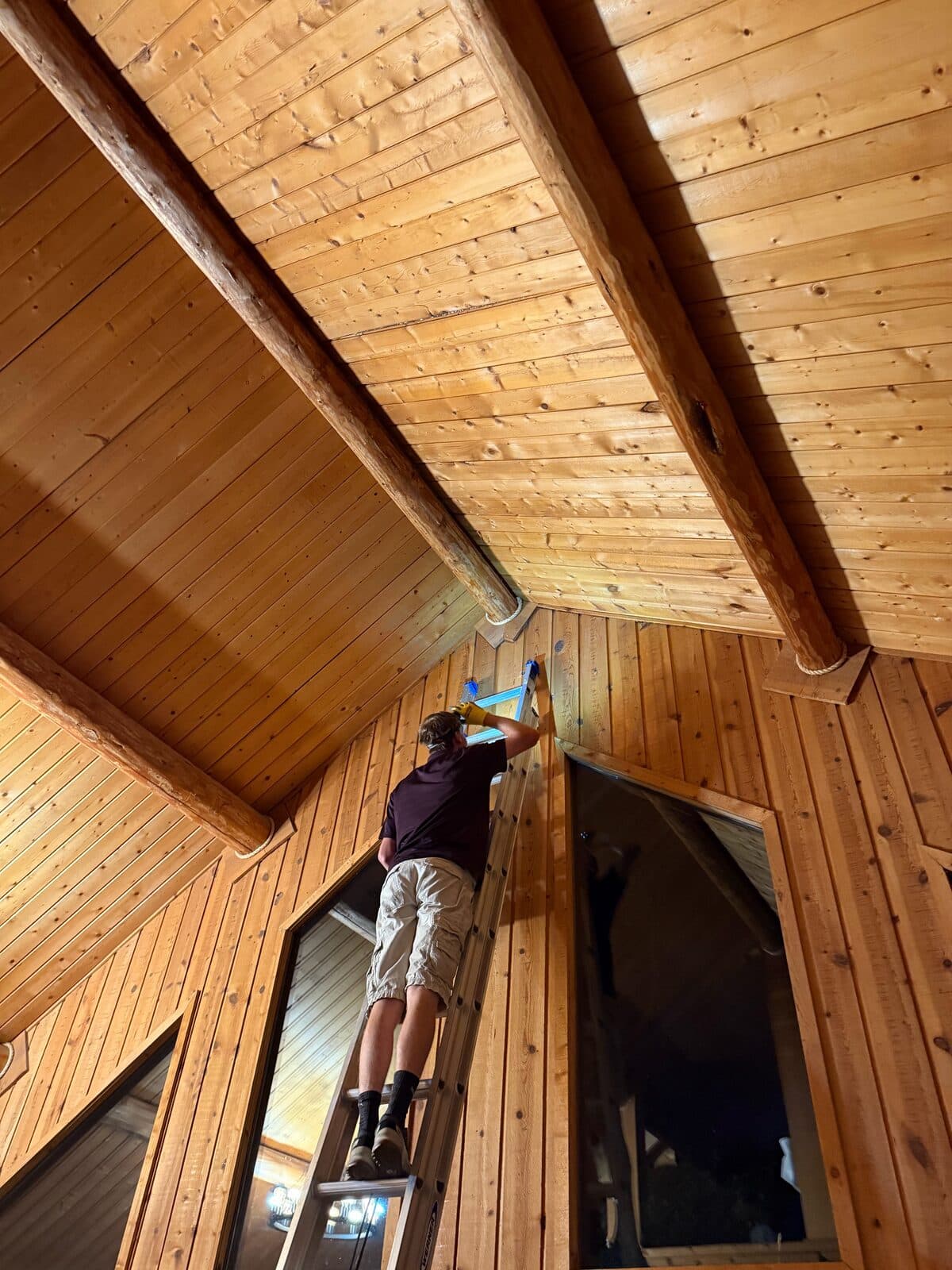 Wood-paneled vaulted ceiling with a technician on a ladder working the peak corner